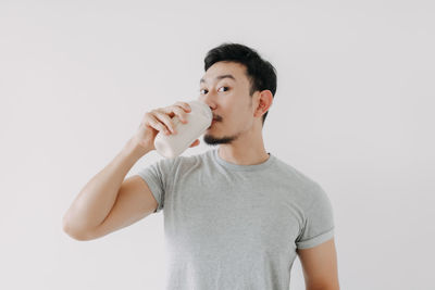 Portrait of smiling young woman drinking milk against white background