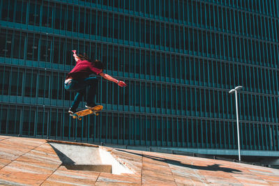 Low angle view of man skateboarding in mid-air against building