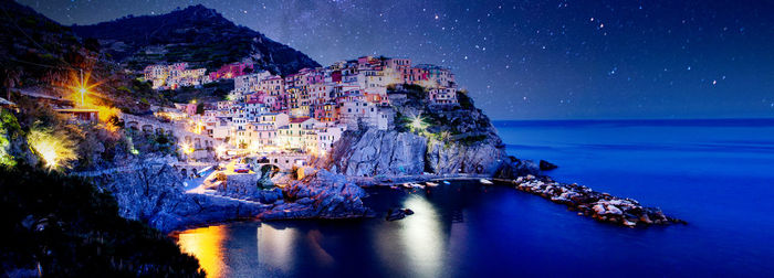 Panoramic view of illuminated rock by sea against sky at night