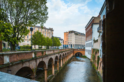 Bridge over river amidst buildings in city against sky