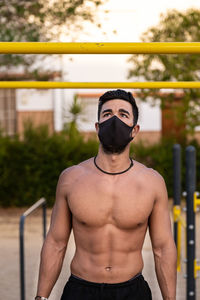 Shirtless man wearing mask exercising at park