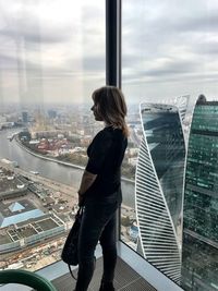 Woman looking at city while standing by window