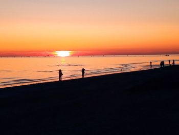 Silhouette people on beach against sky during sunset