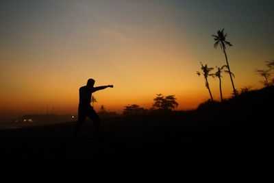 Silhouette man standing on field against sky during sunset