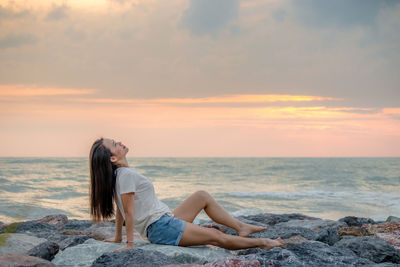 Woman relaxing on beach against sky during sunset