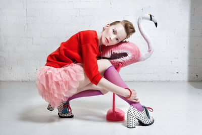 Portrait of mid adult woman posing with flamingo model against wall