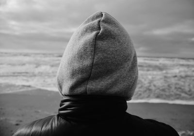 Rear view of person wearing hooded shirt standing at beach