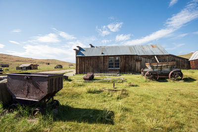 Abandoned built structure on field against sky in ghost town and mining cart