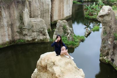 High angle view of woman sitting on cliff by sea