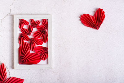 Red paper diy hearts in an empty photo frame and leaves on a concrete background.