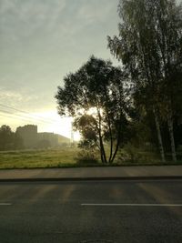 Road by trees against sky during sunset