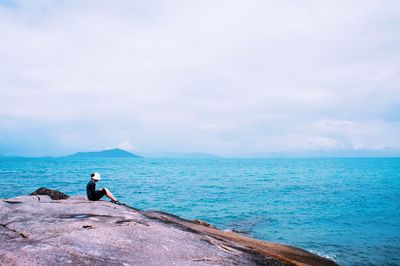 Man sitting on coast against sky