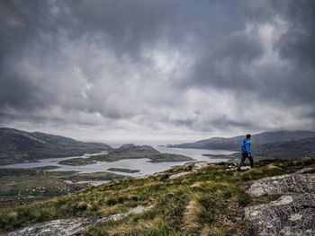 Man walking on mountain road against cloudy sky