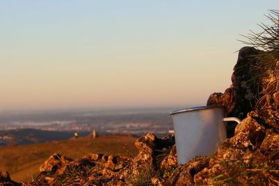 Scenic view of coffee cup on rocks against clear sky during sunrise