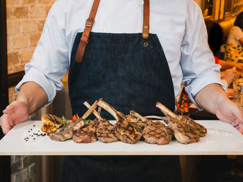 Midsection of chef holding meat on cutting board at restaurant