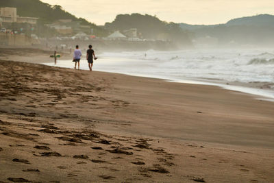 People at beach against sky during sunrise