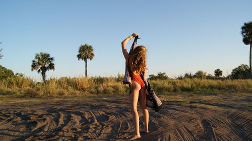 Rear view full length of young woman wearing one piece swimsuit holding scarf on sand
