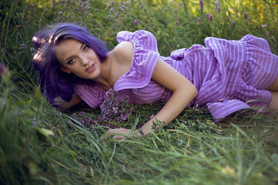 Teenage girl with dyed purple hair and a nose piercing in the grass and in a short dress