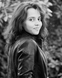 Portrait of smiling young woman wearing leather jacket standing against plants