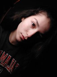 Close-up portrait of young woman against black background