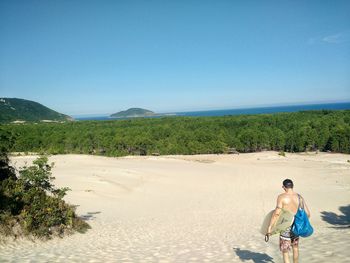 Rear view of shirtless man on beach against sky