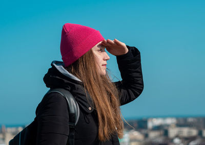 Young confident woman long hair in pink hat black coat. stylish millennial girl walks sky background