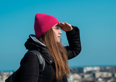 Young woman long hair in pink hat black coat blue sky background. stylish millennial girl walking