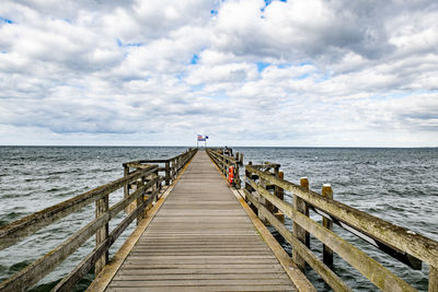 A wooden footbridge leads across the moving sea to the horizon under a thickly clouded sky