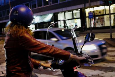 Woman riding motorcycle on city street at night