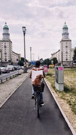 Rear view of man riding bicycle on road against buildings