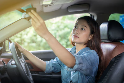 Woman adjusting rear-view mirror while sitting in car