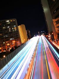 Light trails on road by illuminated buildings in city at night