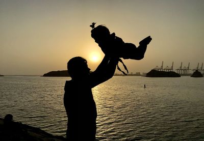 Silhouette man standing at beach against sky during sunset with his daughter.