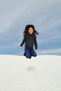 Full length of happy woman jumping on beach against sky