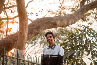 Portrait of young man standing by tree trunk