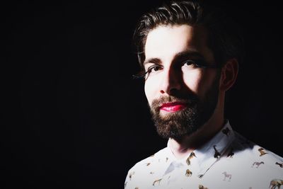 Portrait of man with red lipstick in artificial eyelash against black background