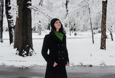 Woman looking up while standing on snow covered road 