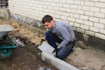 Man laying gray concrete paving slabs in house courtyard on gravel foundation base. master 