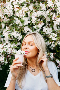 Woman with eyes closed holding cup by flowering plants