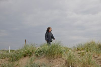 Girl looking away while standing on grass against sky