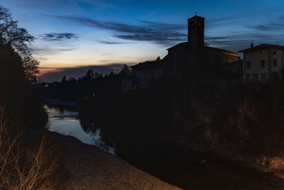 Buildings by river against sky at dusk