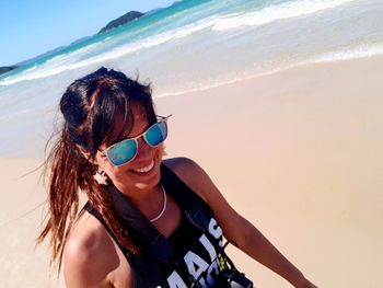 Happy young woman wearing sunglasses while walking at beach during sunny day