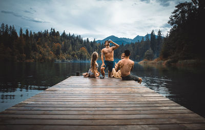 Rear view of people sitting by lake against sky