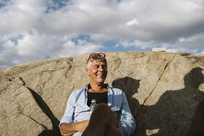 Full length of smiling man standing on rock against sky