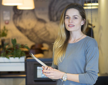 Portrait of confident young woman with clipboard standing in restaurant