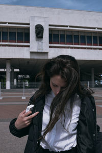 Young woman using mobile phone while standing on building