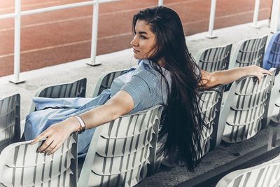 Young woman with long hair sitting on chair at stadium