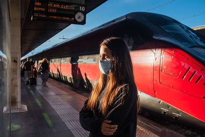 Teenage girl with face mask  checking departure timetable board at railroad station in venice, italy