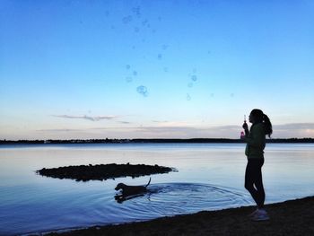 Side view of woman blowing bubbles by dog swimming in lake