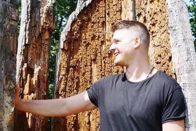 Portrait of young man standing by tree trunk